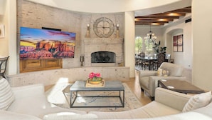 A living room with a fireplace, a television, and a dining area with chairs. - Luxury Estate with Pool, Desert Views & Casita (Cave Creek)