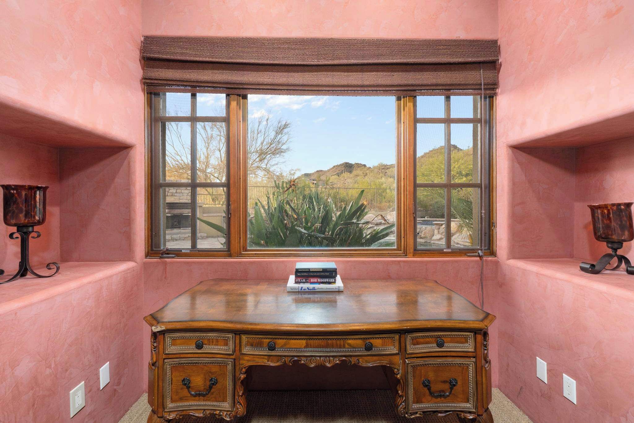 Une chambre d’angle avec un bureau, une fenêtre donnant sur un paysage désertique et deux appliques murales.