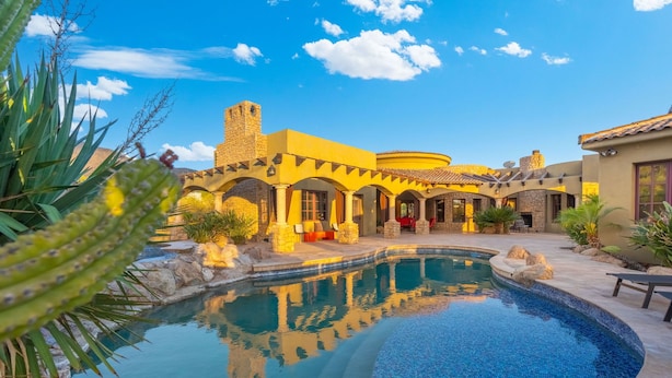 A pool surrounded by a courtyard with stone arches and a stone tower. - Luxury Estate with Pool, Desert Views & Casita (Cave Creek)