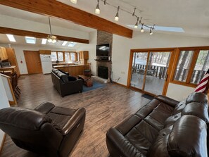 A spacious living area with a fireplace, leather sofas, a kitchen, and a deck with a view. - Hike, Bike & Ski, 12 Mi to Slopes: Serene Cabin-Greer, AZ (Greer)