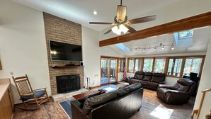 A spacious living room with a fireplace, leather sofas, a TV, and large windows. - Hike, Bike & Ski, 12 Mi to Slopes: Serene Cabin-Greer, AZ (Greer)