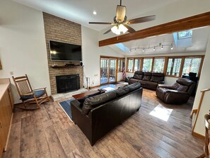 A spacious living room with a fireplace, leather sofas, a TV, and large windows. - Hike, Bike & Ski, 12 Mi to Slopes: Serene Cabin-Greer, AZ (Greer)