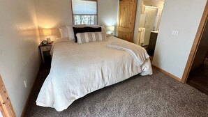 A bedroom with a bed, a nightstand, a lamp, a window, and a door. - Hike, Bike & Ski, 12 Mi to Slopes: Serene Cabin-Greer, AZ (Greer)