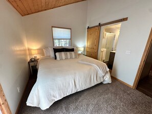 A bedroom with a bed, a nightstand, a lamp, a window, and a door. - Hike, Bike & Ski, 12 Mi to Slopes: Serene Cabin-Greer, AZ (Greer)