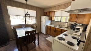 Una cocina compacta con armarios de madera, estufa, refrigerador y una mesa de comedor con sillas.