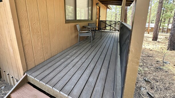Una terraza de madera con una mesa y sillas, una ventana y vistas del bosque circundante.