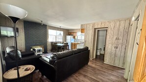 Una sala de estar con sofá, una mesa pequeña, una lámpara y una zona de cocina con mesa y sillas.