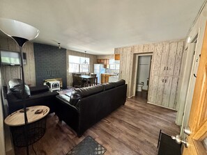 A living room with a sofa, a small table, a lamp, and a kitchen area with a dining table and chairs. - Cozy Cabin in Greer: Hike, Bike & Ski! (Greer)