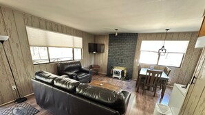 Una sala de estar con un sofá de cuero negro, una chimenea, un televisor y un comedor con una mesa y sillas.