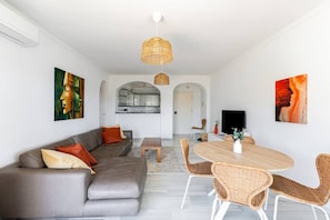 Ein modernes Wohnzimmer mit einem grauen Sofa, Korbstühlen, einem Holzesstisch und Kunstwerken an den Wänden.