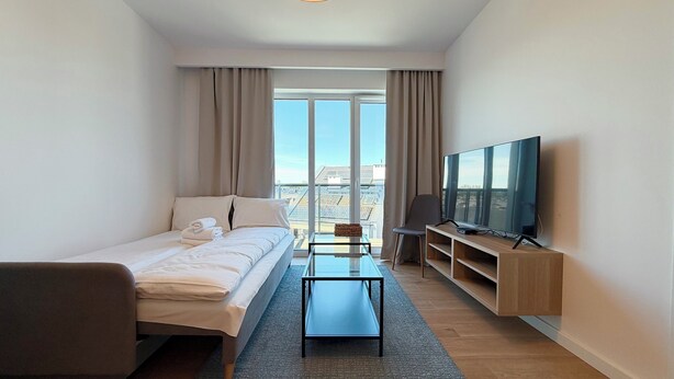 Een moderne hotelkamer met een bed, een televisie, een glazen bijzettafeltje en uitzicht op de stad.