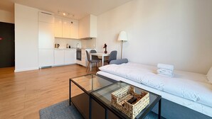 Een moderne, compacte leefruimte met een kitchenette, een glazen salontafel, een bank en een lamp.