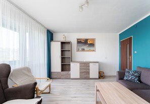 A modern living room with a sofa, a coffee table, a chair, a cabinet, and a painting on the wall. - Park Zakrzówek Homely Apartment (Kraków)