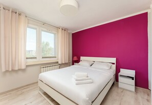 A bedroom with a bed, a nightstand, a window with curtains, and a radiator. - Park Zakrzówek Homely Apartment (Kraków)