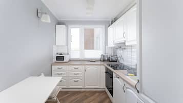 Een moderne keuken met witte kastjes, een magnetron, een spoelbak en een eethoek met een tafel.