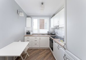 A modern kitchen with white cabinets, a microwave, a sink, and a dining area with a table. - Park Zakrzówek Homely Apartment (Kraków)