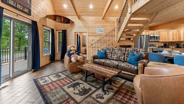 L’intérieur d’un chalet en bois, avec un canapé, un ours en peluche, une table à manger et un coin cuisine.