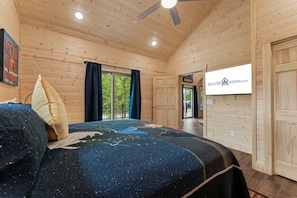 Ein Schlafzimmer einer Holzhütte mit Bett, Deckenventilator, Fenster mit Vorhängen und einer Tür.