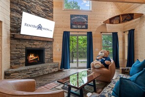 Ein Blockhaus-Interieur mit Kamin aus Stein, einem Schild mit der Aufschrift 'Thunder Cabin Table Rock Lake' und einem großen Teddybären auf einem Sofa.