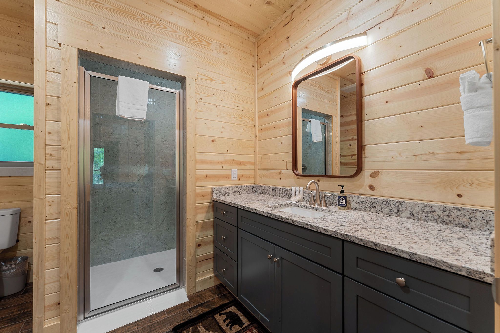 A wooden interior with a shower, a sink with a mirror, and cabinets.