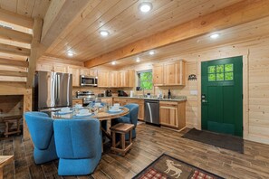A wooden cabin interior with a dining area, kitchen, and a green door.