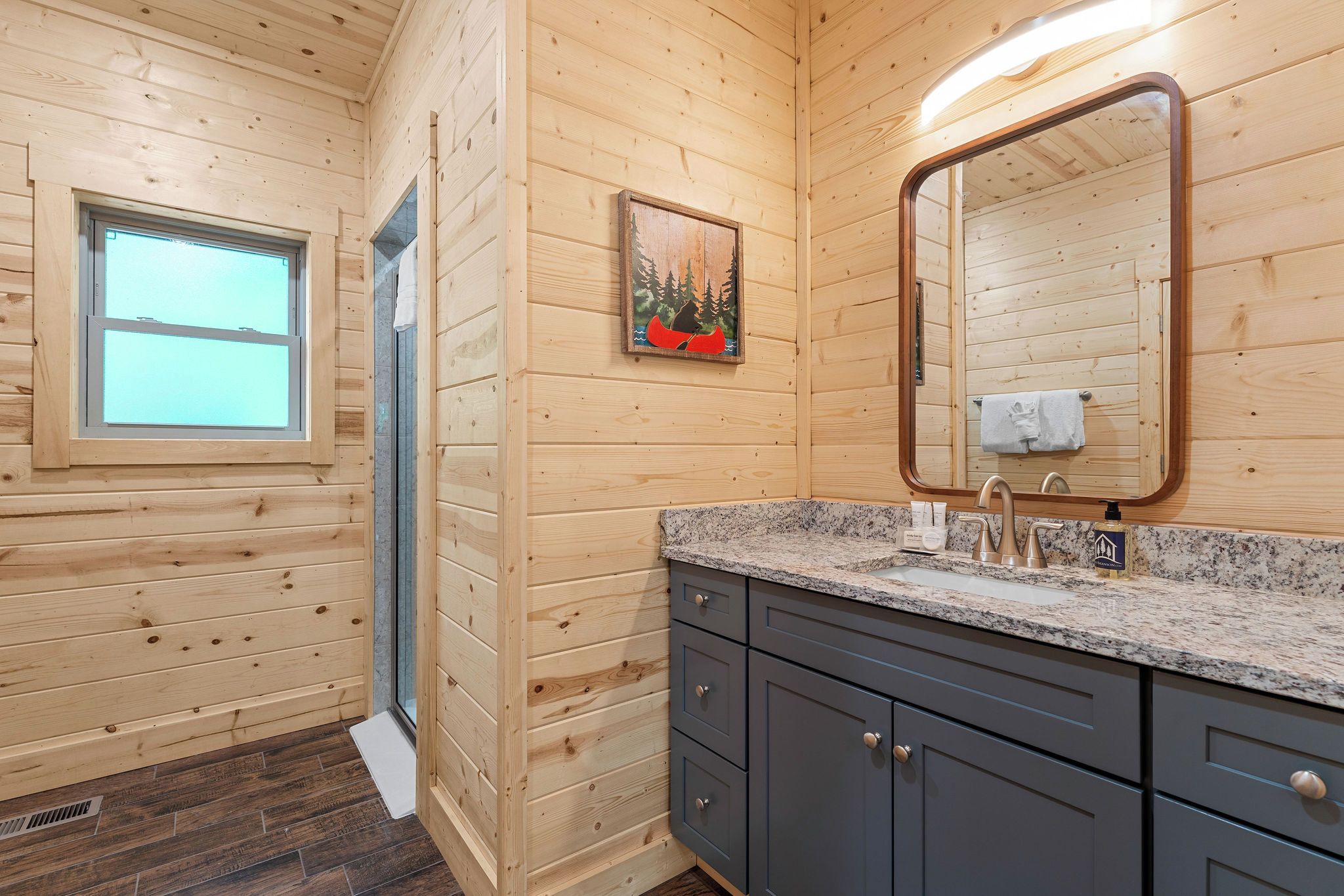 A wooden cabin bathroom with a granite countertop, a sink, and a mirror.