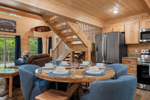 Een chaletinterieur met een eettafel voor vier personen, een keuken met moderne apparatuur, en een trap naar een hoger niveau.