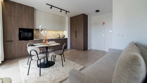 Ein modernes Wohnzimmer mit einer Couch, einem Essbereich mit Stühlen und einem Tisch, einer Küche mit Einbauofen sowie einem wandmontierten Flachbildfernseher.
