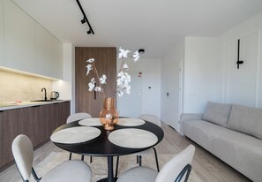 Una sala de estar moderna con una mesa de comedor redonda, un sofá color beige y un florero con flores blancas.