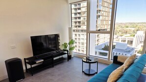 Un salon moderne avec une grande télévision, un canapé, une petite table et une plante en pot.