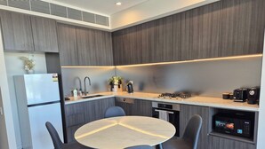 Une cuisine moderne avec des meubles de couleur grise, un plan de travail blanc, un four encastré et une table de salle à manger ronde, accompagnée de quatre chaises.