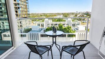 A balcony with two chairs and a small table, overlooking a cityscape with modern buildings and greenery.
