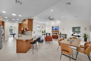 A spacious kitchen with a central island, dining area with chairs, and a fireplace.