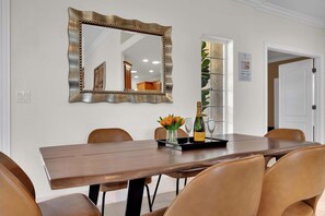 Un comedor con una mesa de madera, sillas, un espejo y una bandeja con una botella y flores.