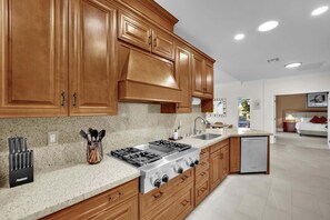 A modern kitchen with wooden cabinets, a gas stove, a dishwasher, and a granite countertop.