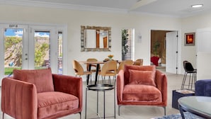 A hotel room with a dining area, two red velvet armchairs, a mirror, and a door leading outside.