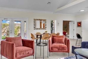 A hotel room with a dining area, two red velvet armchairs, a mirror, and a door leading outside.