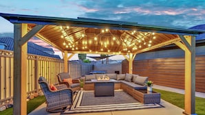 An outdoor patio with a wooden pergola, seating area, and string lights.