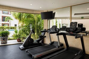 A gym with treadmills, exercise bikes, and a TV screen. - Gated community in Playacar | Pool, Golf and Beach (Playa del Carmen)