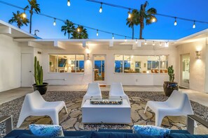Eine Terrasse im Freien mit weißen Stühlen, einer Feuerstelle und Lichterketten.