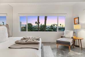 Ein modernes Schlafzimmer mit großem Fenster, einem Bett, einem Sessel und einem kleinen Tisch.