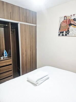 A bedroom with a wooden wardrobe, a bed with white linens, and a wall-mounted artwork. - Charming 1-bedroom Apartment in South B, Nairobi (Nairobi)