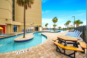 A swimming pool with lounge chairs and picnic tables, surrounded by palm trees and a building. - Seaside Escape 2 Queen Efficiency in Sand Dunes Resort (Myrtle Beach)