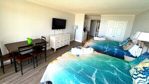 Habitación de hotel con una cama, un escritorio, una silla, un aparador, un televisor y un baño visible al fondo.