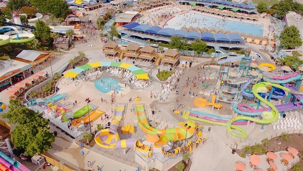 A water park with various slides and pools, surrounded by buildings and trees.