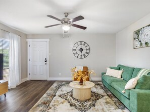 A living room with a ceiling fan, a clock, a green sofa, a coffee table with a vase, and a patterned rug. - FIFA 2026 | AT&T Stadium | Six Flags 1 Free Parking (Arlington)