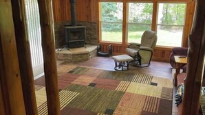 A cozy room with a stone fireplace, a large window, and a patterned rug.