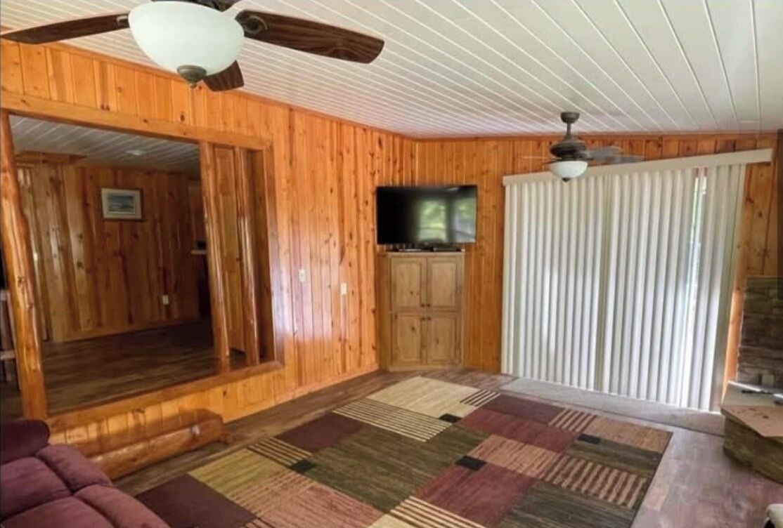 A wooden interior with a ceiling fan, a television, and a patterned rug.