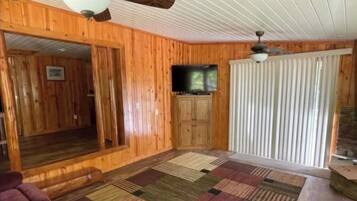 A wooden interior with a ceiling fan, a television, and a patterned rug.