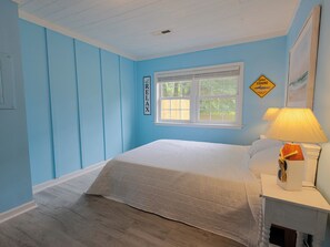 Ein Schlafzimmer mit Bett, Fenster, einem an der Wand befestigten Schild und einer Lampe.